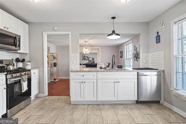 kitchen with hanging light fixtures, sink, tasteful backsplash, white cabinetry, and stainless steel appliances