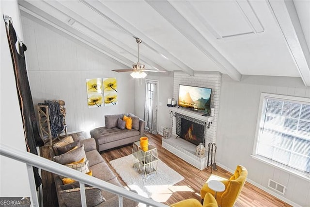 living room with ceiling fan, lofted ceiling with beams, a brick fireplace, and wood-type flooring