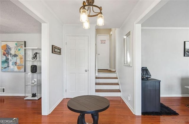 corridor featuring hardwood / wood-style flooring, a textured ceiling, ornamental molding, and an inviting chandelier