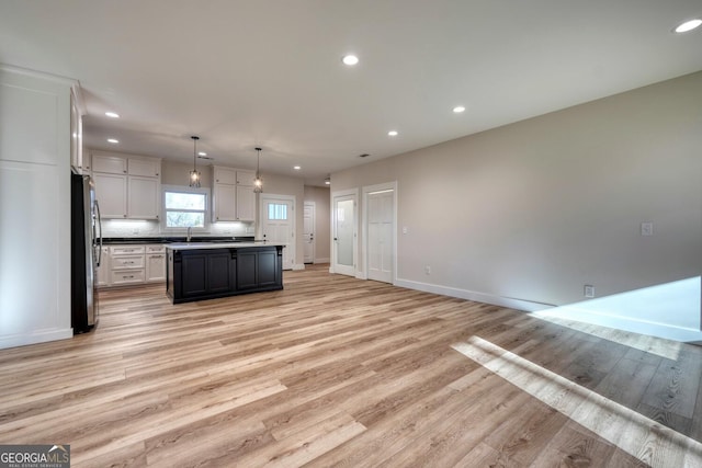 kitchen featuring white cabinetry, hanging light fixtures, light hardwood / wood-style flooring, and stainless steel fridge