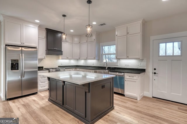 kitchen with a kitchen island, white cabinets, hanging light fixtures, and appliances with stainless steel finishes