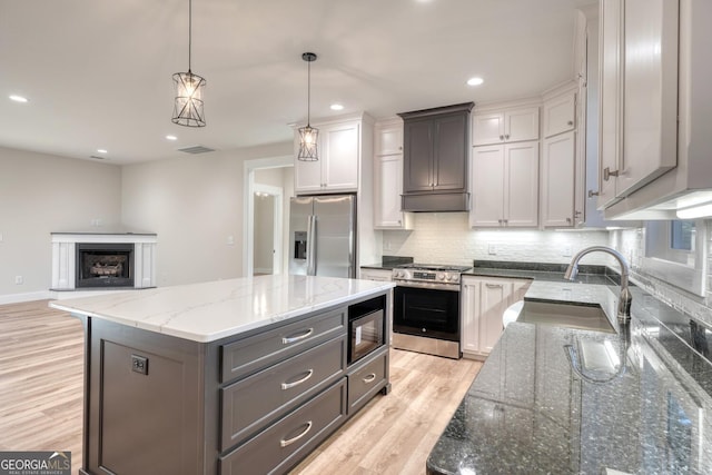 kitchen featuring a kitchen island, decorative light fixtures, stainless steel appliances, dark stone counters, and sink