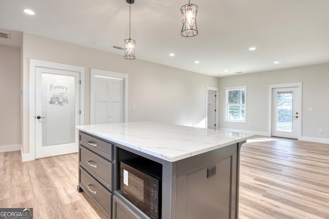 kitchen with hanging light fixtures, gray cabinetry, a kitchen island, light hardwood / wood-style flooring, and light stone counters