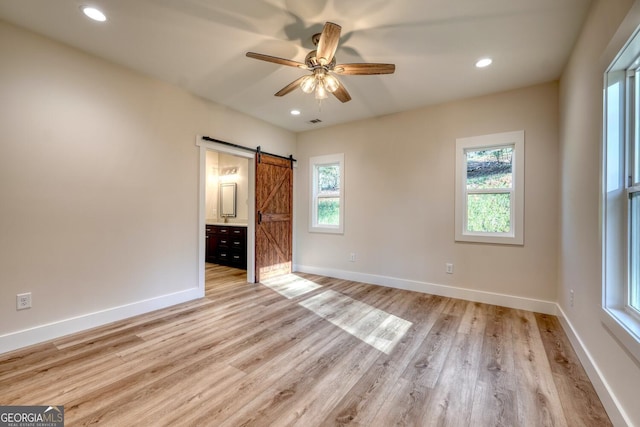 interior space with ceiling fan, multiple windows, connected bathroom, and a barn door