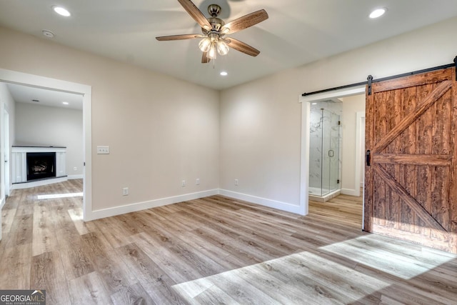 spare room featuring ceiling fan, a barn door, and light hardwood / wood-style flooring