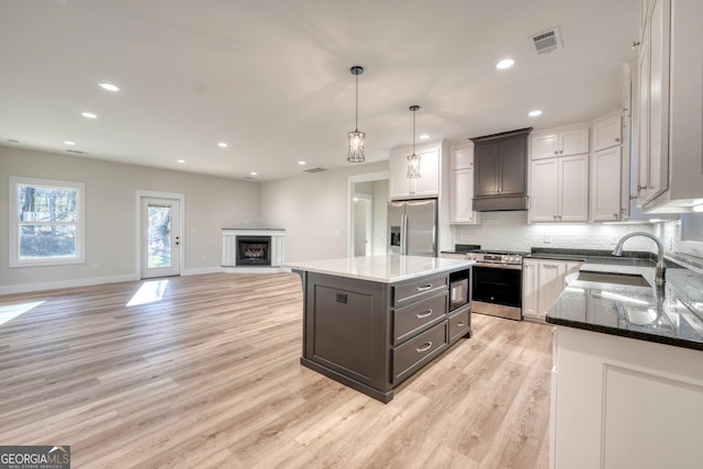 kitchen with appliances with stainless steel finishes, a kitchen island, decorative light fixtures, sink, and light hardwood / wood-style flooring