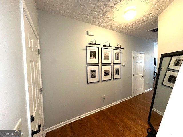 corridor with a textured ceiling and dark hardwood / wood-style flooring