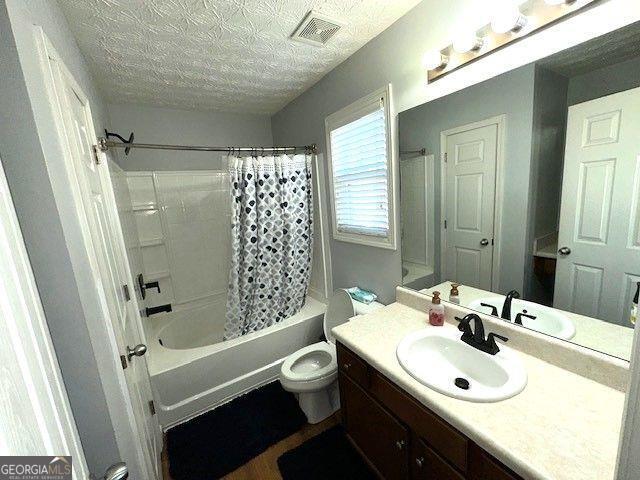 full bathroom with shower / bath combo with shower curtain, a textured ceiling, toilet, and vanity