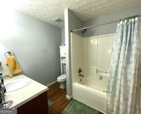 full bathroom featuring shower / bath combo, hardwood / wood-style flooring, a textured ceiling, toilet, and vanity