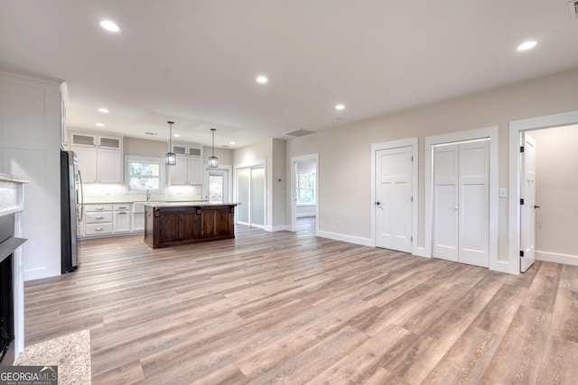 kitchen with a center island, white cabinetry, stainless steel refrigerator, light hardwood / wood-style flooring, and pendant lighting