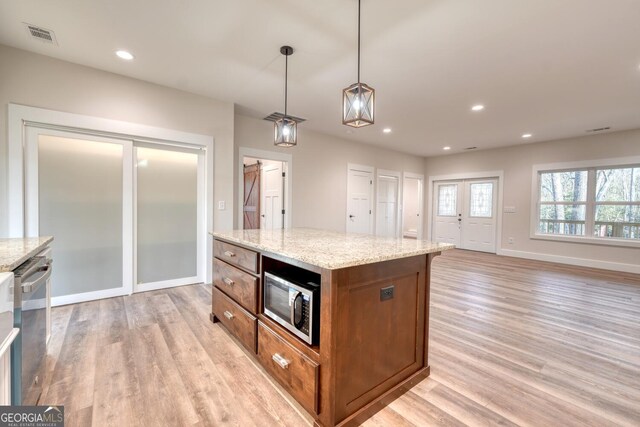 kitchen featuring a kitchen island, light stone countertops, hanging light fixtures, and stainless steel appliances