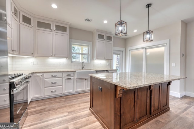 kitchen featuring stainless steel gas range oven, sink, white cabinetry, and a kitchen island