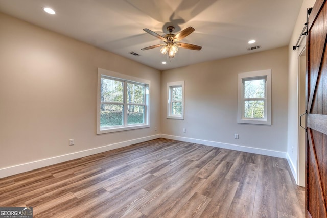 empty room featuring light wood-type flooring, plenty of natural light, and a barn door