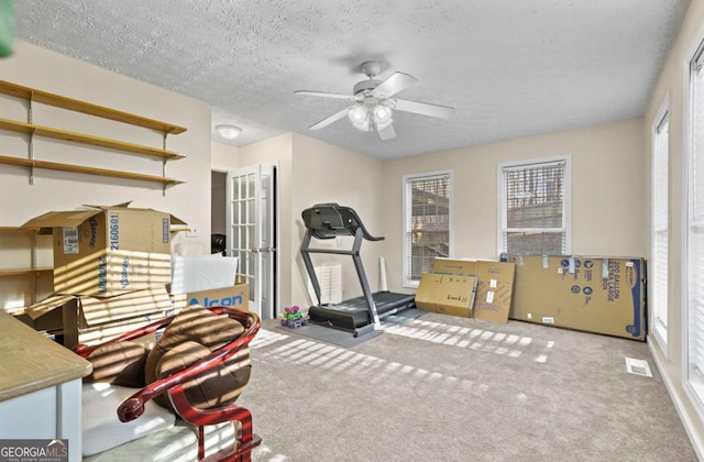 workout area featuring ceiling fan, carpet flooring, and a textured ceiling