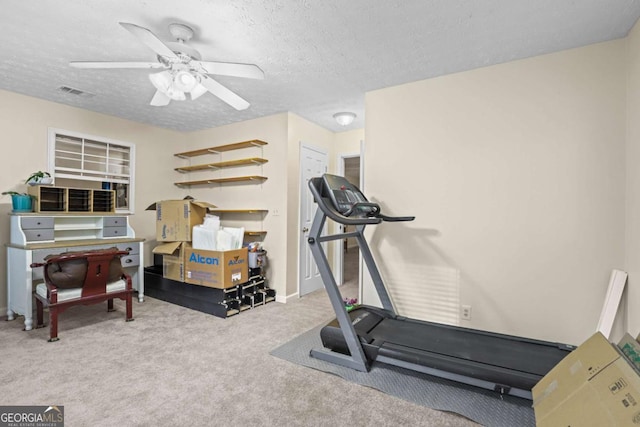 exercise area featuring ceiling fan, light colored carpet, and a textured ceiling