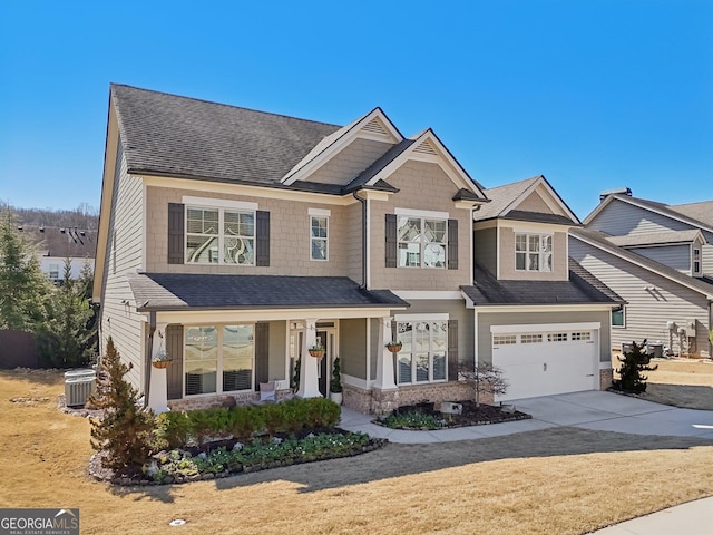 view of front facade featuring a shingled roof, concrete driveway, covered porch, an attached garage, and central AC unit