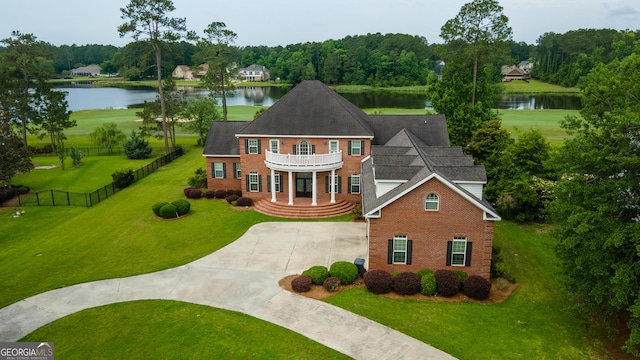 view of front facade featuring a balcony, a water view, and a front lawn