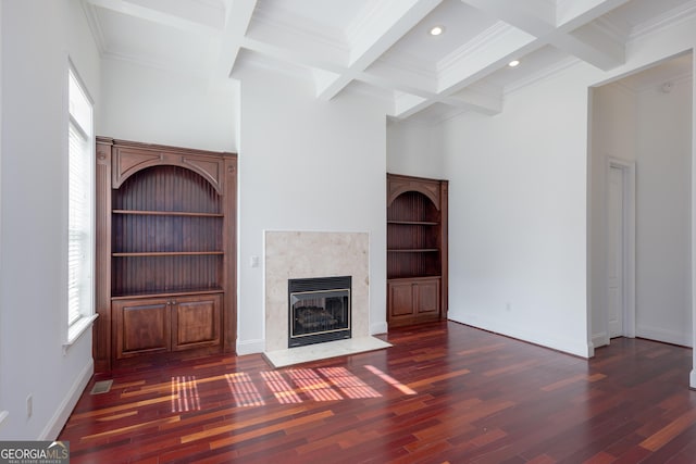 unfurnished living room featuring dark wood-type flooring, beam ceiling, a tiled fireplace, and coffered ceiling