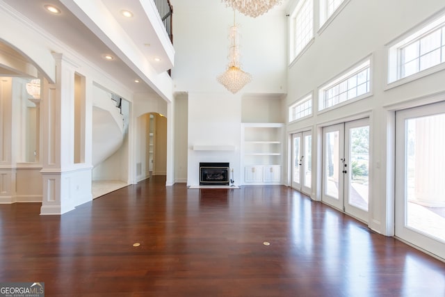 unfurnished living room featuring built in features, a towering ceiling, french doors, and dark wood-type flooring