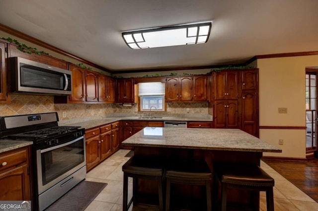 kitchen featuring a center island, crown molding, appliances with stainless steel finishes, light tile patterned floors, and a breakfast bar