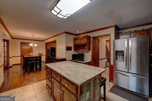 kitchen with crown molding, decorative light fixtures, stainless steel fridge with ice dispenser, light tile patterned flooring, and a center island