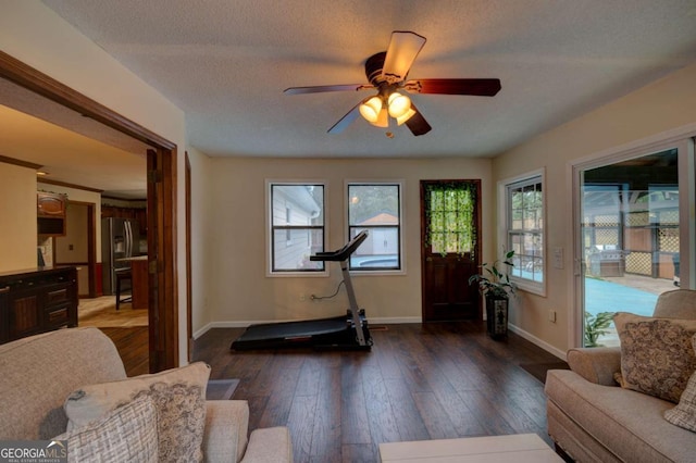 workout room with ceiling fan, dark wood-type flooring, and a textured ceiling