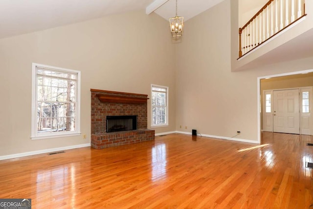 unfurnished living room featuring a brick fireplace, a wealth of natural light, wood-type flooring, and beam ceiling