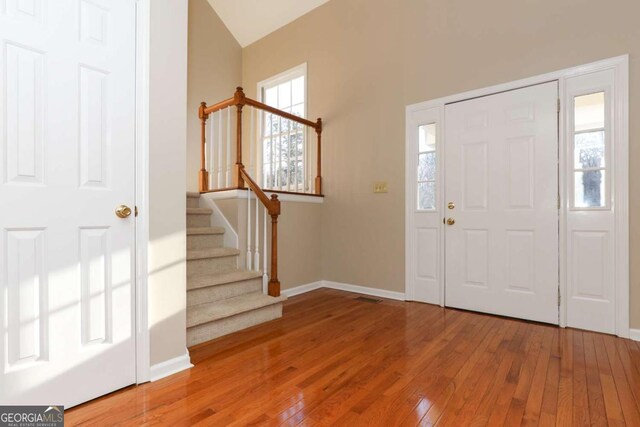 foyer featuring baseboards, vaulted ceiling, hardwood / wood-style flooring, and stairs
