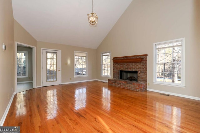 unfurnished living room with high vaulted ceiling, baseboards, a fireplace, and light wood-style flooring