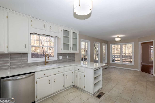kitchen featuring stainless steel dishwasher, a peninsula, light countertops, a sink, and backsplash