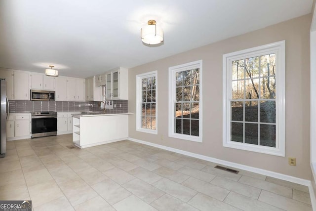 kitchen featuring kitchen peninsula, appliances with stainless steel finishes, white cabinets, light tile patterned floors, and decorative backsplash