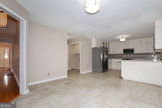 kitchen with white cabinets, a sink, stainless steel appliances, baseboards, and backsplash