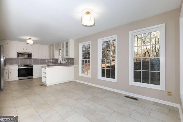 kitchen featuring backsplash, visible vents, light countertops, glass insert cabinets, and stainless steel appliances
