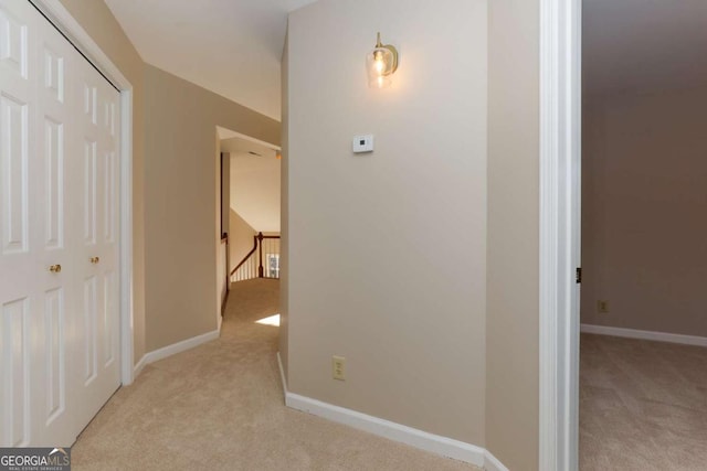 corridor with baseboards, an upstairs landing, and light colored carpet