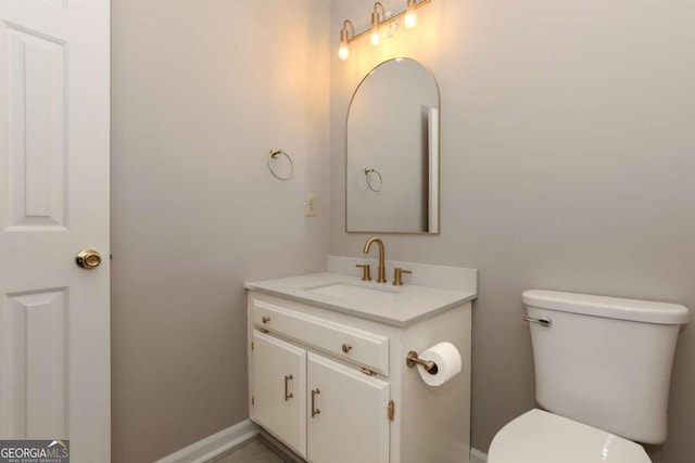 half bathroom with vanity, baseboards, and toilet