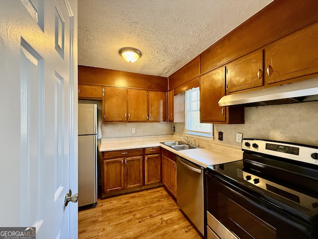 kitchen with sink, stainless steel appliances, light hardwood / wood-style floors, and a textured ceiling