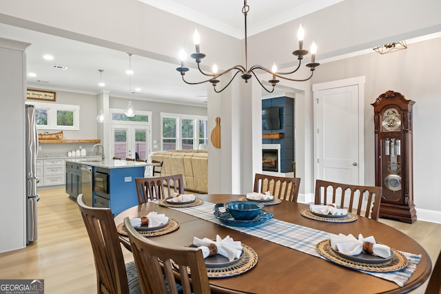 dining area featuring light hardwood / wood-style flooring, french doors, sink, ornamental molding, and a large fireplace