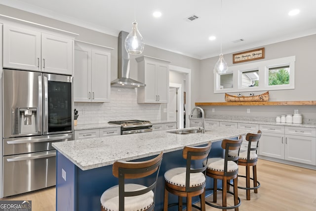 kitchen featuring appliances with stainless steel finishes, sink, white cabinetry, a kitchen island with sink, and wall chimney range hood