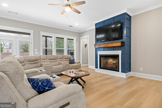 living room featuring ceiling fan, light hardwood / wood-style flooring, ornamental molding, and a fireplace