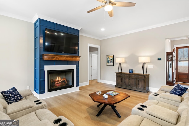 living room featuring ceiling fan, a large fireplace, light hardwood / wood-style flooring, and ornamental molding