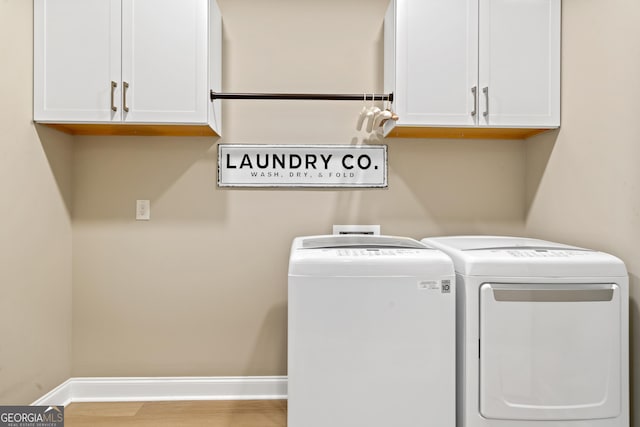 clothes washing area with cabinets, wood-type flooring, and washing machine and clothes dryer