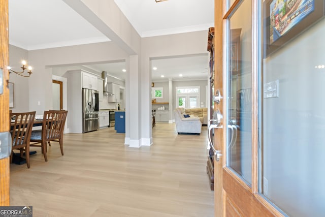 foyer entrance with an inviting chandelier, ornamental molding, and light wood-type flooring