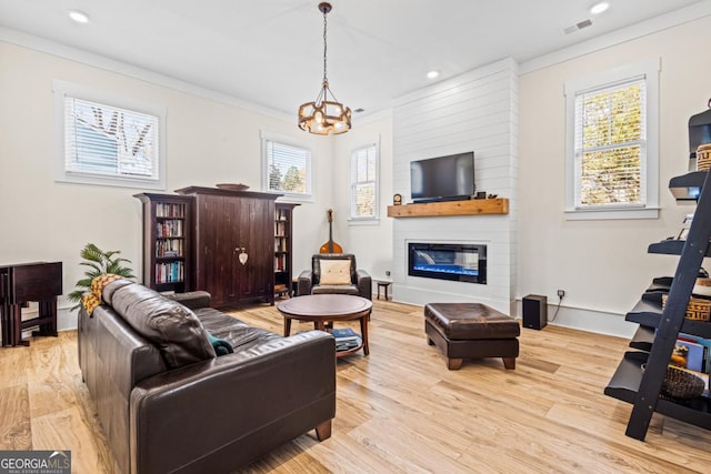 living room featuring crown molding, light wood-type flooring, a chandelier, and a large fireplace