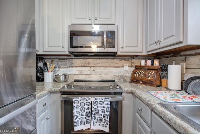 kitchen with light stone counters, backsplash, white cabinets, and stainless steel appliances