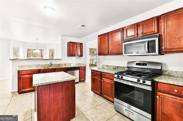 kitchen with pendant lighting, appliances with stainless steel finishes, light tile patterned floors, light stone counters, and a center island