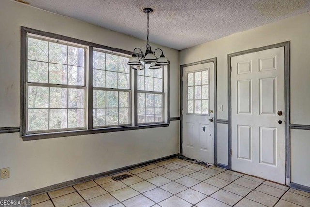 unfurnished dining area featuring a textured ceiling, light tile patterned floors, and an inviting chandelier