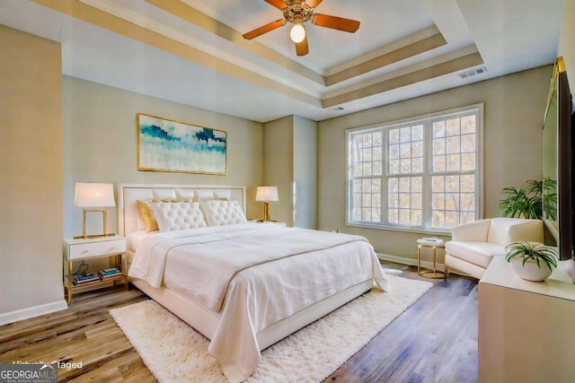 bedroom featuring ceiling fan, wood-type flooring, a tray ceiling, and crown molding