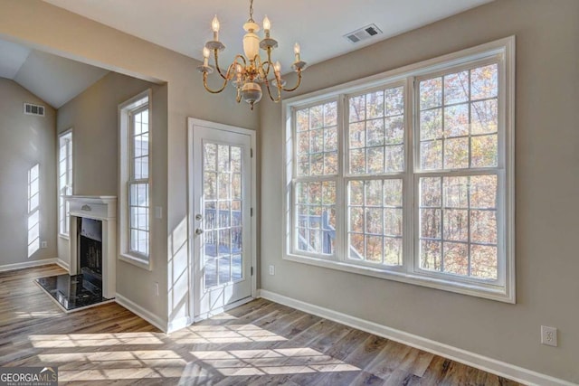 doorway to outside with hardwood / wood-style floors, a healthy amount of sunlight, vaulted ceiling, and a notable chandelier