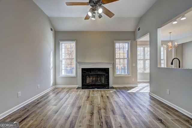 unfurnished living room with wood-type flooring, sink, a premium fireplace, ceiling fan with notable chandelier, and lofted ceiling