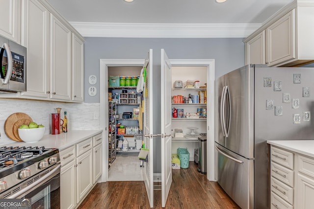 kitchen featuring tasteful backsplash, dark wood finished floors, light countertops, ornamental molding, and stainless steel appliances